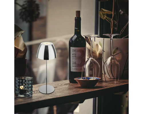 Dekorative Tischleuchte aus Metall neben einer Flasche Wein und Gläsern auf einem Tisch.