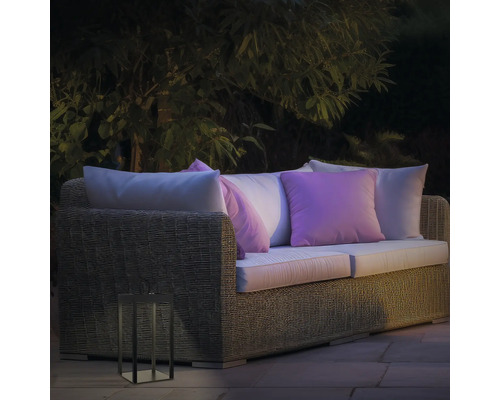 Gartenszene mit Rattan-Lounge-Sofa, Kissen und dekorativer Laterne für den Außenbereich