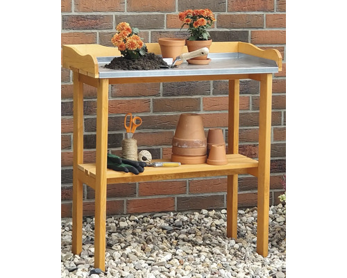 Gartentisch mit Ablagefläche und Gartenzubehör wie Töpfe, Blumenerde, Handschuhe, Schere und Pflanzkelle.