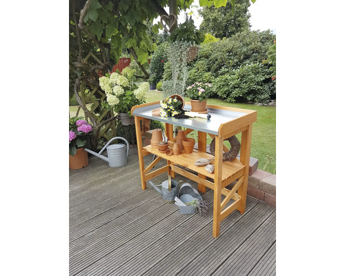 Gartenszene mit einem Pflanztisch aus Holz, verschiedenen Töpfen und Gießkannen.