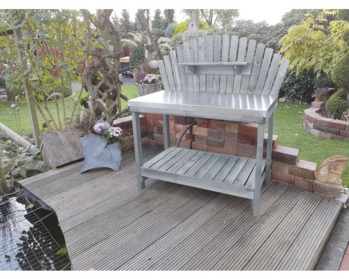 Gartenszene mit einem grauen Pflanztisch mit Metalloberfläche und Holzregal im Freien