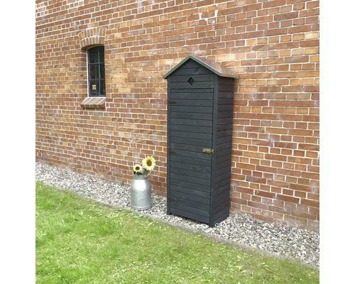 Geräteschrank aus Holz vor einer Backsteinmauer mit einem Milchkanne und Sonnenblumen.