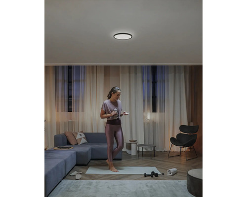 Wohnzimmer mit Deckenleuchte, Couch und trainierender Frau