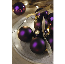 Dekorative violette Weihnachtskugeln mit goldenen Bändern auf einem Teller mit Lichtern