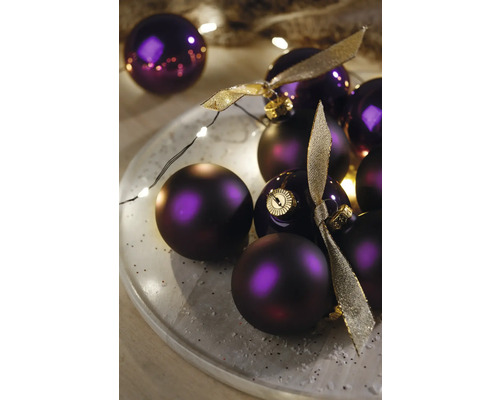 Dekorative violette Weihnachtskugeln mit goldenen Bändern auf einem Teller mit Lichtern