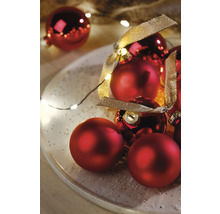 Dekorative Anordnung von roten Weihnachtskugeln mit Bändern und Lichterkette auf einem Teller