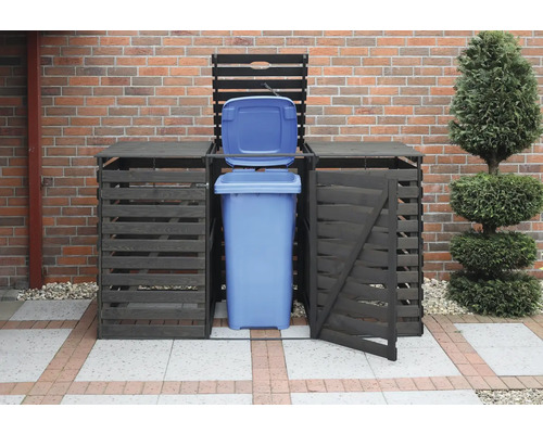 Mülltonnenbox mit geöffneter blauer Mülltonne vor einer Backsteinmauer