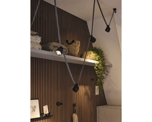 Innenaufnahme eines Raumes mit einer Pendelleuchte mit mehreren Strahlern und Textilkabeln vor einer Wandverkleidung.