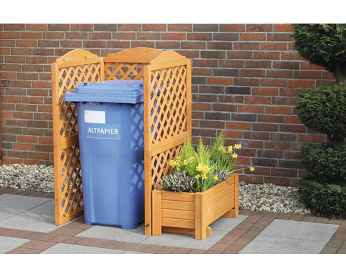 Mülltonnenbox aus Holz mit Gitterstruktur neben einer blauen Papiermülltonne und einem bepflanzten Holzkasten
