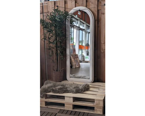 Dekorative Szene mit einem Spiegel mit Bogenrahmen, einer Kunstpflanze und einem Schaffell auf einer Holzpalette