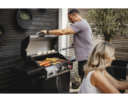 Mann grillt mit einem Gasgrill im Garten. Auf dem Grill liegen Gemüse und Fleisch.