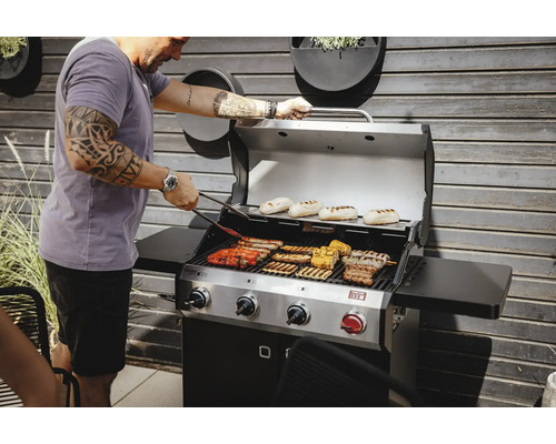 Mann grillt verschiedene Speisen auf einem Gasgrill im Freien.