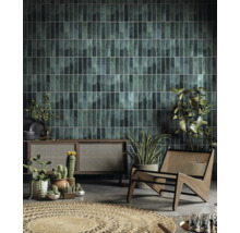 Wohnzimmer mit grünen Wandfliesen, Holzschrank, Korbstuhl und Pflanzen