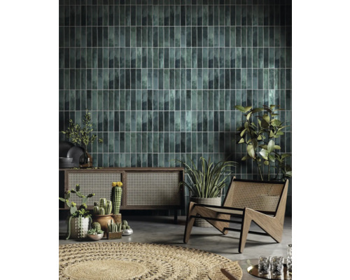 Wohnzimmer mit grünen Wandfliesen, Holzschrank, Korbstuhl und Pflanzen