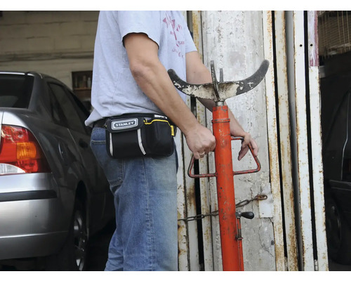 Eine Person mit einer Werkzeugtasche der Marke Stanley und einer Getriebestütze.