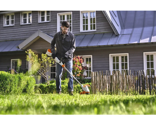 Mann verwendet einen Akku-Rasentrimmer im Garten.
