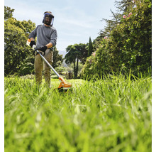 Mann mit Schutzhelm und Motorsense beim Rasenmähen im Garten.