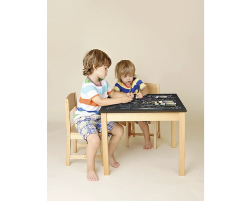 Zwei Kinder sitzen an einem Kindertisch mit Stühlen und malen mit Stiften auf der Tischplatte.