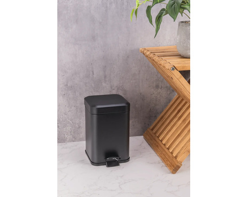 Schwarzer Treteimer aus Metall neben einem Holzhocker mit Pflanze