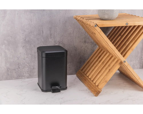 Schwarzer Treteimer aus Metall neben einem Tritthocker aus Holz.