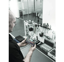 Eine Person hält ein Wera Tool-Check Plus 1 Werkzeugset vor einer Werkzeugwand.