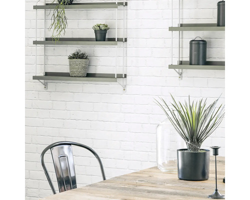 Wohnraum mit Wandregalen, Tisch und Stuhl vor einer weißen Ziegelwand