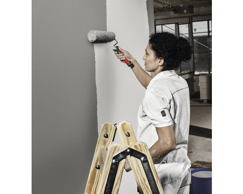 Frau streicht Wand mit Farbroller auf einer Leiter stehend
