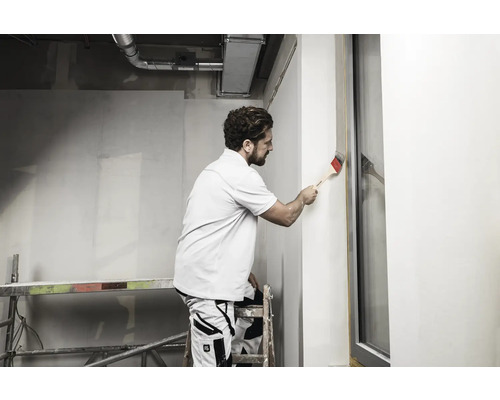 Mann streicht Wand mit Pinsel auf einer Baustelle