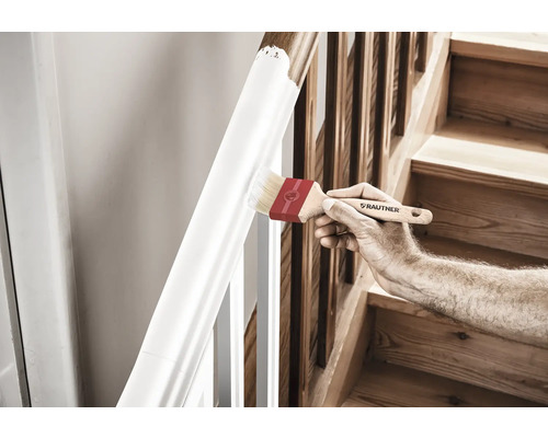 Eine Person streicht ein Treppengeländer mit einem Pinsel.