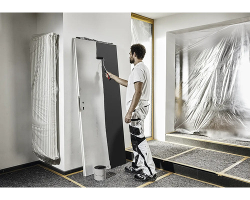 Ein Mann streicht eine Tür mit einer Farbrolle in einem Raum, der mit Folie abgedeckt ist