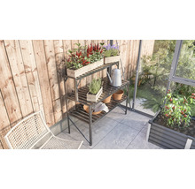 Gartenszene mit dreistufigem Pflanztisch aus Metall, bepflanzt mit Kräutern und Blumen, Gießkanne und Gartenhandschuhen
