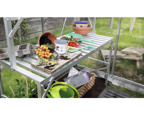 Gewächshaus mit Pflanztisch, Töpfen und Gartengeräten.