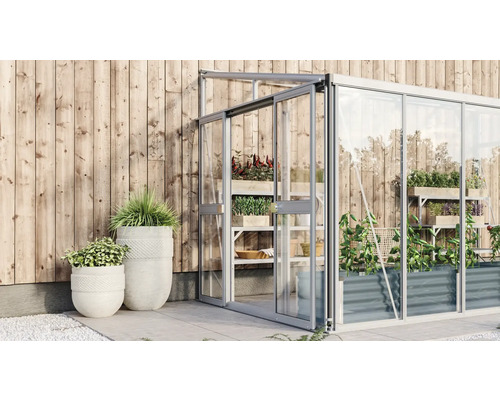 Gewächshaus mit Pflanzen und Pflanzgefäßen vor Holzwand