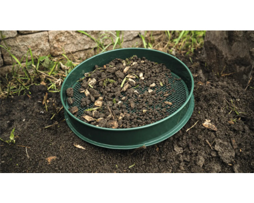 Gartensieb mit Erde und Pflanzenresten auf dem Boden