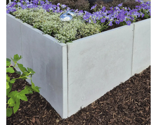 Hochbeet aus Beton mit blühenden Pflanzen im Garten.