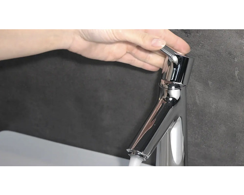 Hand betätigt einen Wasserhahn aus Metall.