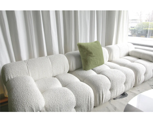 Weißes modulares Sofa mit Kissen und Strukturbezug vor einem Fenster mit Vorhängen