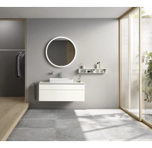 Badezimmer mit Waschtisch, rundem Spiegel mit Beleuchtung und Ablageflächen.