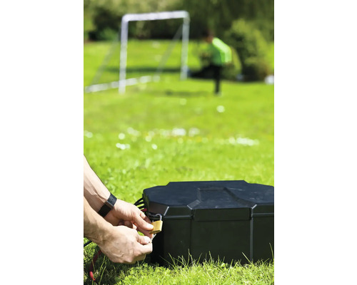 Person schließt eine schwarze Outdoor-Strombox mit Vorhängeschloss auf einer Rasenfläche ab.