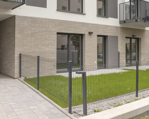 Drahtzaun vor einem modernen Wohngebäude mit Rasenfläche