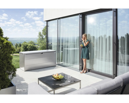 Aufbewahrungsbox StyleBox Gr. 140 Biohort 398 l 40 x 60 x 71 cm silber-metallic Szene mit einer Aufbewahrungsbox aus Metall auf einer Terrasse, einem Tisch und einer Frau, die Weintrauben isst