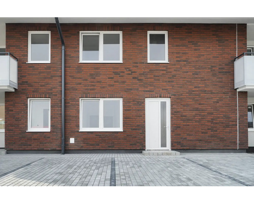 Fassade eines Hauses mit Ziegelmauerwerk, weißen Fenstern und einer Tür
