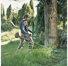 Mann arbeitet mit einer Motorsense im Garten und trägt dabei Schutzkleidung.