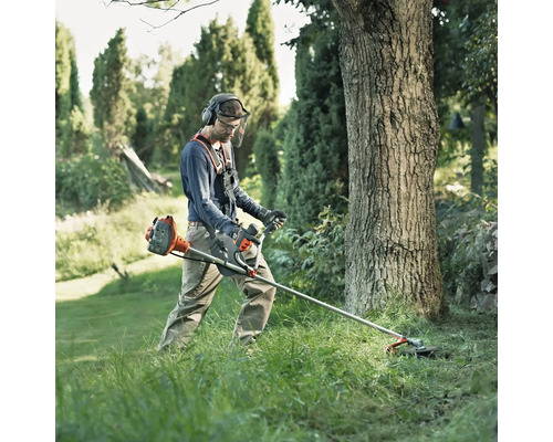 Mann arbeitet mit einer Motorsense im Garten und trägt dabei Schutzkleidung.