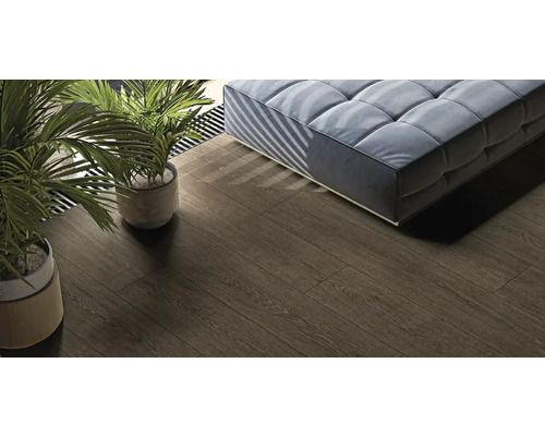 Feinsteinzeug Wand- und Bodenfliese Nordic Wood 19,8 cm x 120 cm x 0,9 cm choco matt rektifiziert Ansicht eines Zimmers mit Holzboden, Couch und Zimmerpflanzen.