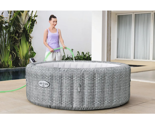 Aufblasbarer Lay-Z-Spa Bali Whirlpool mit geflochtener Optik und einer Person, die ihn mit einem Schlauch befüllt.