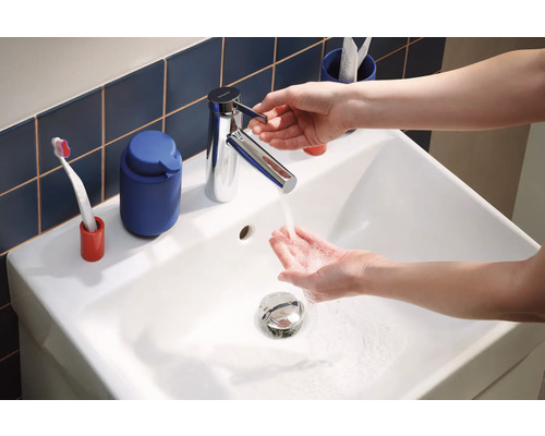 Waschbecken mit Armatur und laufendem Wasser, im Hintergrund Badaccessoires