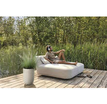 Mann entspannt auf einer Gartenliege mit Kopfhörern, neben ihm ein Pflanzgefäß mit Ziergras auf einer Holzterrasse.