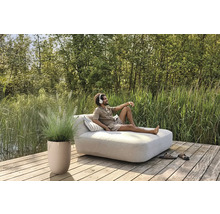 Szene mit Mann auf einer Gartenliege mit Kissen, Topfpflanze und Schuhen auf einer Holzterrasse am See