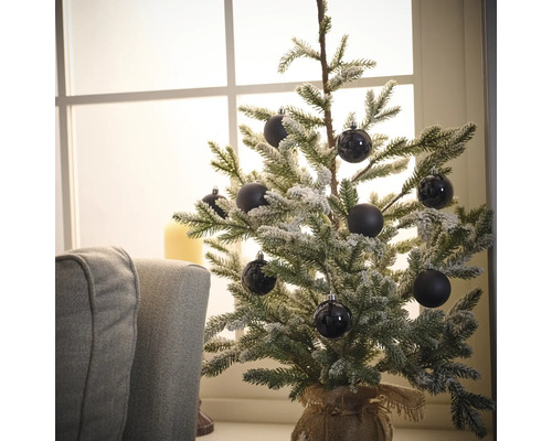 Dekorativer, schneebedeckter Weihnachtsbaum mit schwarzen Kugeln auf einem Tisch in der Nähe eines Fensters